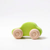 A small green Grimm's Colored Wooden Cars toy with natural wood wheels sits on a white surface against a plain white background.