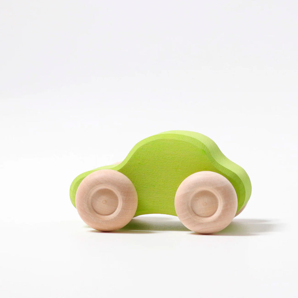 A small green Grimm's Colored Wooden Cars toy with natural wood wheels sits on a white surface against a plain white background.