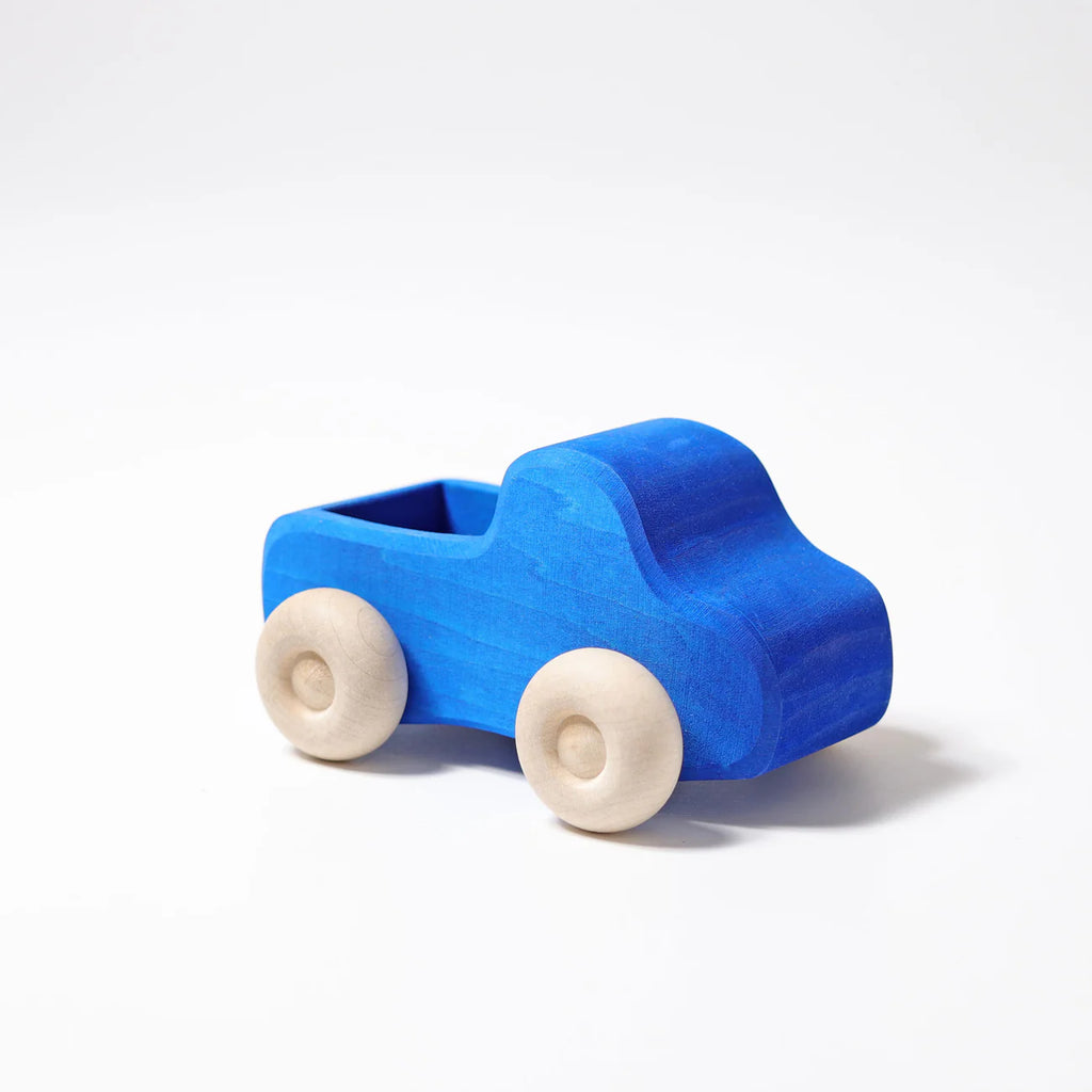 Grimm's Small Blue Truck, crafted from non-toxic wood and featuring natural wood-colored wheels, is pictured against a plain white background. Perfectly sized for little hands, this small blue toy truck encourages imaginative play with its rugged vehicle design.