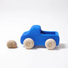 A small brown snail shell sits next to a Grimm's Small Blue Truck—winner of the Spielgut award—with white wheels, on a plain white background.
