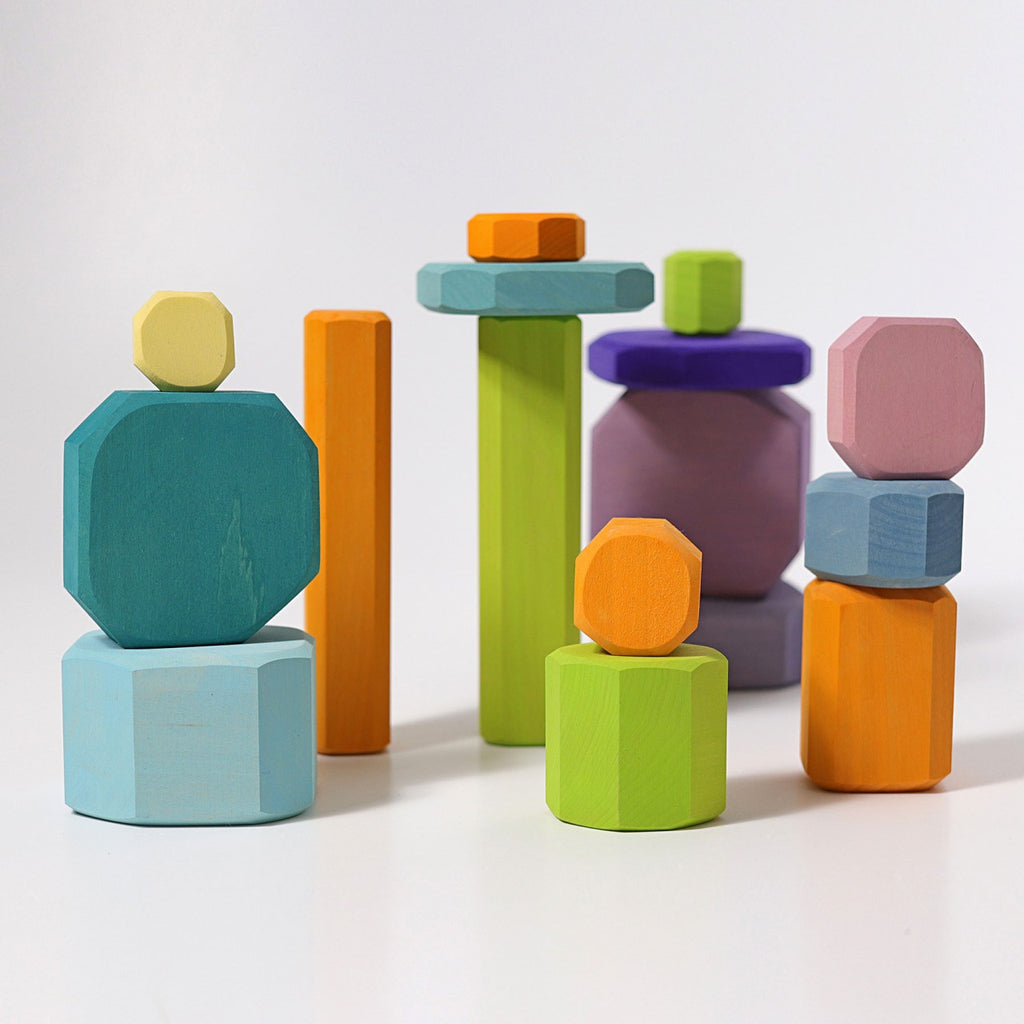 Presenting Grimm's Tree Slices Building Blocks, a vibrant collection of non-toxic wooden stackable pieces featuring an array of geometric shapes and sizes in striking shades of blue, orange, green, yellow, pink, and purple. These colorful building blocks can be balanced vertically to create abstract structures against a plain white backdrop, making them perfect for young children.