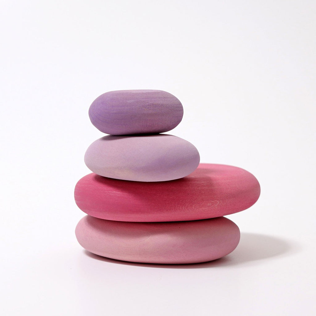 A stack of smooth, rounded Grimm's Flamingo Pebbles Stacker painted in soft pastel shades of pink, purple, and lavender are balanced on top of each other against a plain white background. These non-toxic toys not only delight the eyes but also provide a fun balance game for all ages.