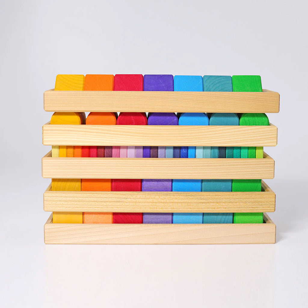 Grimm's Shapes and Colors Set features multicolored geometric building blocks in four wooden trays, each displaying a rainbow gradient from red to green—perfect for developing fine motor skills.