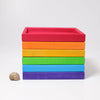 Grimm's Rainbow Frames (coming soon) are stacked in a vibrant gradient beside a small snail shell, perfect for adding color to any kids' workspace, all displayed on a plain white background.