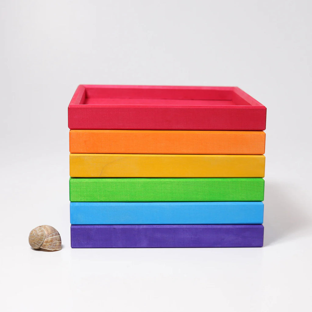 Grimm's Rainbow Frames (coming soon) are stacked in a vibrant gradient beside a small snail shell, perfect for adding color to any kids' workspace, all displayed on a plain white background.