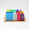 Grimm's Houses, a collection of vibrant wooden toy houses arranged on a wooden board, inspires the imagination of a city planner. The houses, featuring shades of blue, green, yellow, red, purple, and orange with minimalist white line details for doors and windows, evoke the structured liveliness of contemporary urban settings.