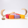 Grimm's Red Hearts Building Blocks: A colorful wooden puzzle with various shapes, including red, orange, purple, and yellow pieces, arranged on a light wooden base. Curved wooden arches and two small seashells are placed nearby on a white background. This non-toxic set helps develop fine motor skills while engaging young minds.