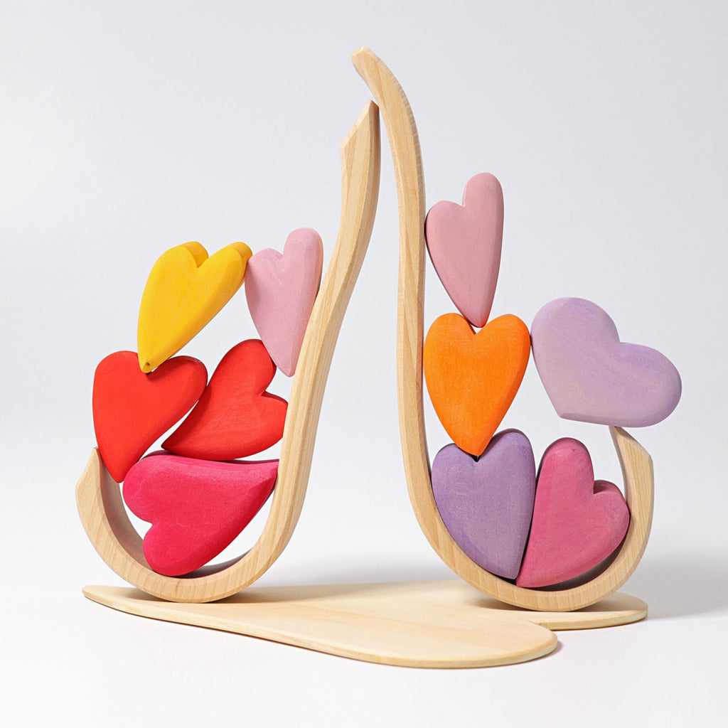 A Grimm's Red Hearts Building Blocks with a natural finish is stacked with colorful heart-shaped blocks in shades of yellow, red, pink, and purple. The hearts are arranged in a symmetrical, cascading pattern, creating a playful and aesthetically pleasing design that enhances fine motor skills.