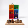 A collection of pinecones and acorns on a wooden board, with a Grimm’s Small 6 Piece Rainbow Box Sorter in the background.