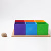 Grimm’s Small 6 Piece Rainbow Box Sorter featuring six rainbow-colored wooden storage boxes arranged on a wooden tray, with a small snail shell sitting to the left.