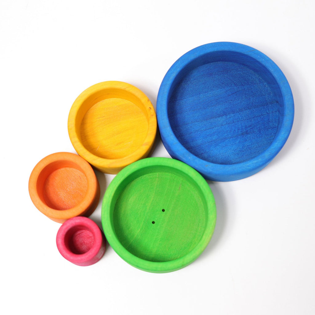 Grimm's Rainbow Stacking Bowls Blue to Red features five round wooden bowls in varying sizes and colors—blue, green, yellow, orange, and red—arranged in a cluster. Made with natural non-toxic stain, these bowls are a charming stacking toy.