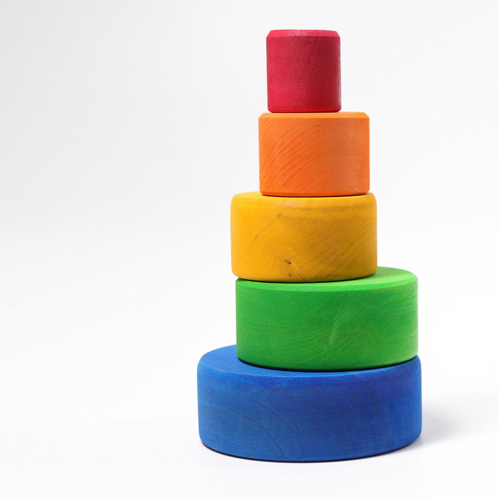 Grimm's Rainbow Stacking Bowls Blue to Red features five colorful, round wooden bowls—blue, green, yellow, orange, and red—with a natural non-toxic finish, stacked in a pyramid against a plain white background.
