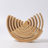 An arrangement of alder-wood crescent-shaped pieces in graduating sizes, forming a semi-circular pattern. The pieces are nested together, creating a layered and symmetrical design against a plain white background, resembling a Grimm's Large Natural Rainbow Stacker constructed of non-toxic materials.