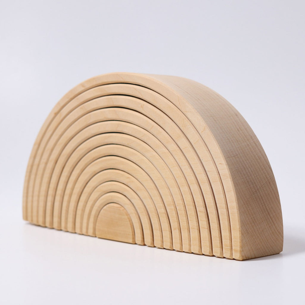 A stackable wooden arch toy, crafted from non-toxic alder-wood, features semicircular pieces of varying sizes, arranged from largest at the base to smallest at the center. Each piece fits neatly within the next, forming a Grimm's Large Natural Rainbow Stacker with a cohesive half-circle structure against a plain white background.