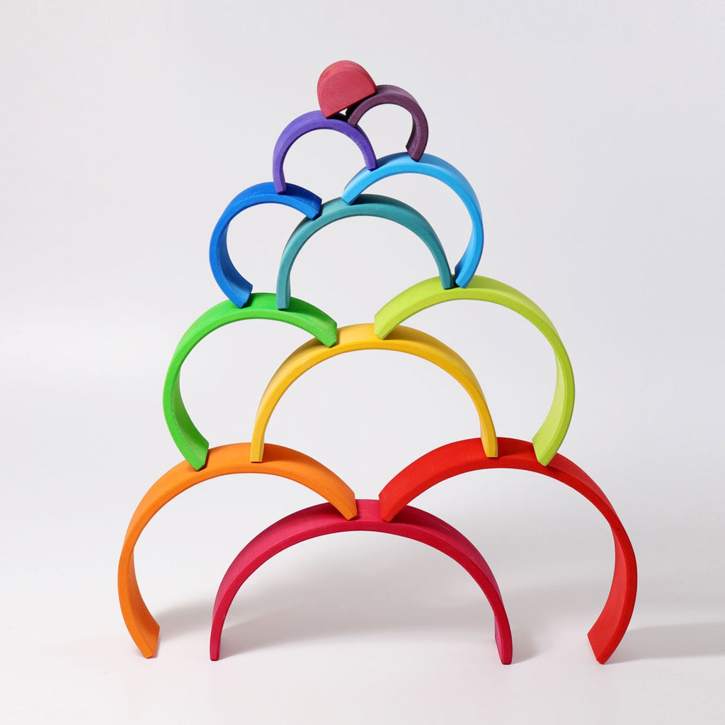 A vibrant and whimsical Grimm's Large Wooden Rainbow displayed in a pyramid arrangement. Each arch, handcrafted from non-toxic wood, features vivid colors: red, orange, yellow, green, blue, purple, and pink. This versatile toy adds a visually appealing touch against a white background.