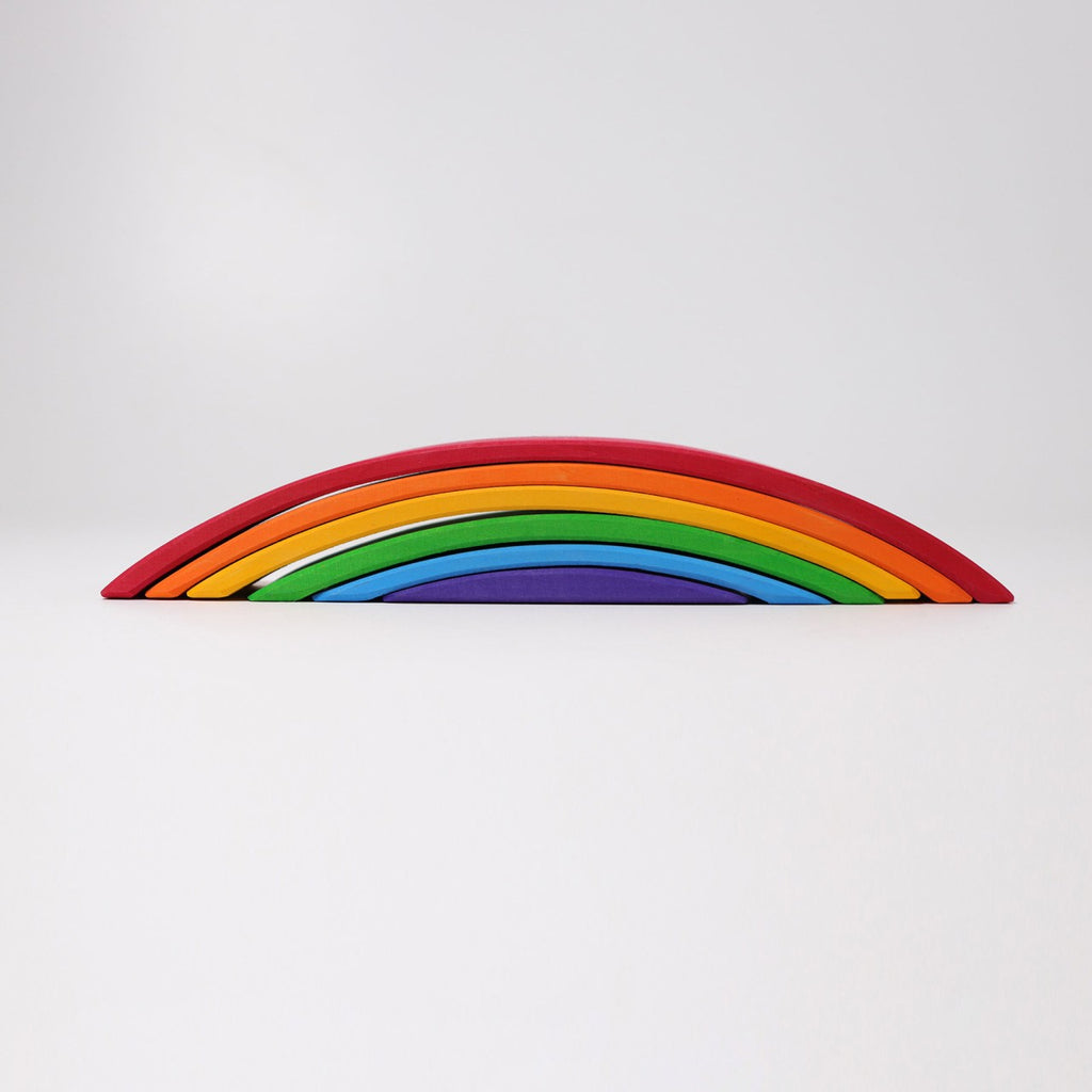 A minimalist image features Grimm's Rainbow Bridge composed of six vibrant arcs: red, orange, yellow, green, blue, and purple. The arcs are arranged in a semi-circle against a plain, light-grey background. This non-toxic toy evokes the charm of a Rainbow Bridge with its vivid hues.