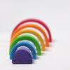 The Grimm's Wooden Rainbow is a versatile toy featuring colorful, semi-circular wooden arches of varying sizes, arranged in a gradient pattern from purple at the front to red at the back. Made from non-toxic wood and laid out on a white background, it promises safe and imaginative play.