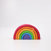 The Grimm's Wooden Rainbow, a vibrant and colorful stacking toy shaped like a rainbow tunnel, is arranged on a white background. Crafted from non-toxic wood, the toy features seven arched pieces in red, orange, yellow, green, blue, and purple that are stacked from largest to smallest in size order.