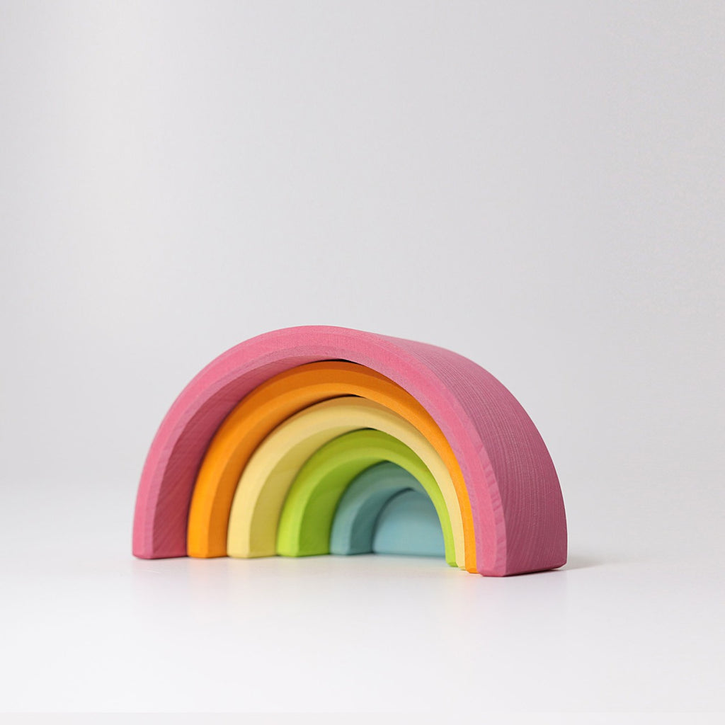 A Grimm's Rainbow Pastel Stacker featuring five nested arches in varying colors, from pink on the outside to blue on the inside. Made with non-toxic materials, it is perfect for toddlers to stack. The toy is displayed on a white surface with a simple, light gray background.