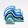 A set of Grimm's Ocean Waves, featuring abstract waterwave shapes in blue and teal, crafted from lime wood, is arranged from smallest to largest against a white background.