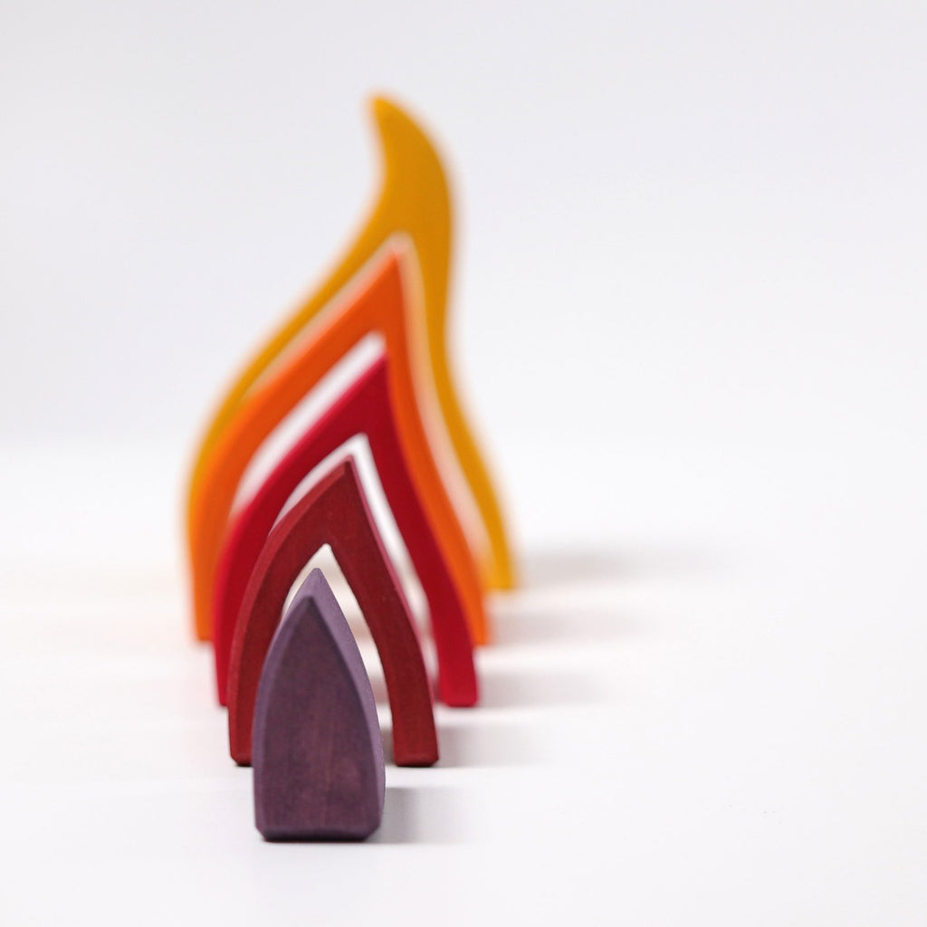 The Grimm's Fire Stacker consists of colorful, curved wooden pieces primarily in shades of yellow, orange, and red, arranged in an abstract, branching pattern against a white background. This charming wooden stacking toy also features a small purple piece shaped like a truncated cone placed in the foreground.