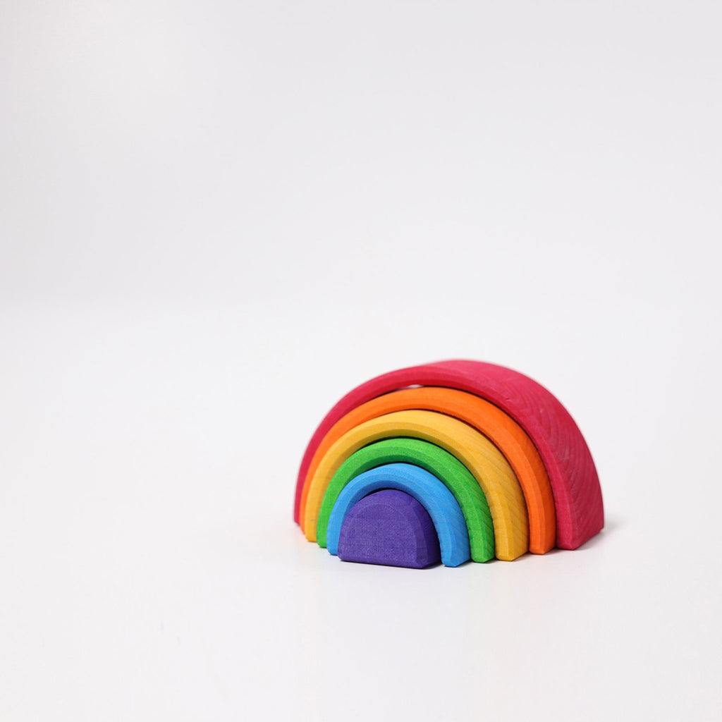 A Grimm's Small Wooden Rainbow, made from non-toxic wood, features seven arched pieces in various colors arranged in a semi-circle on a white background. This versatile toy showcases the colors red, orange, yellow, green, blue, indigo, and violet from top to bottom.