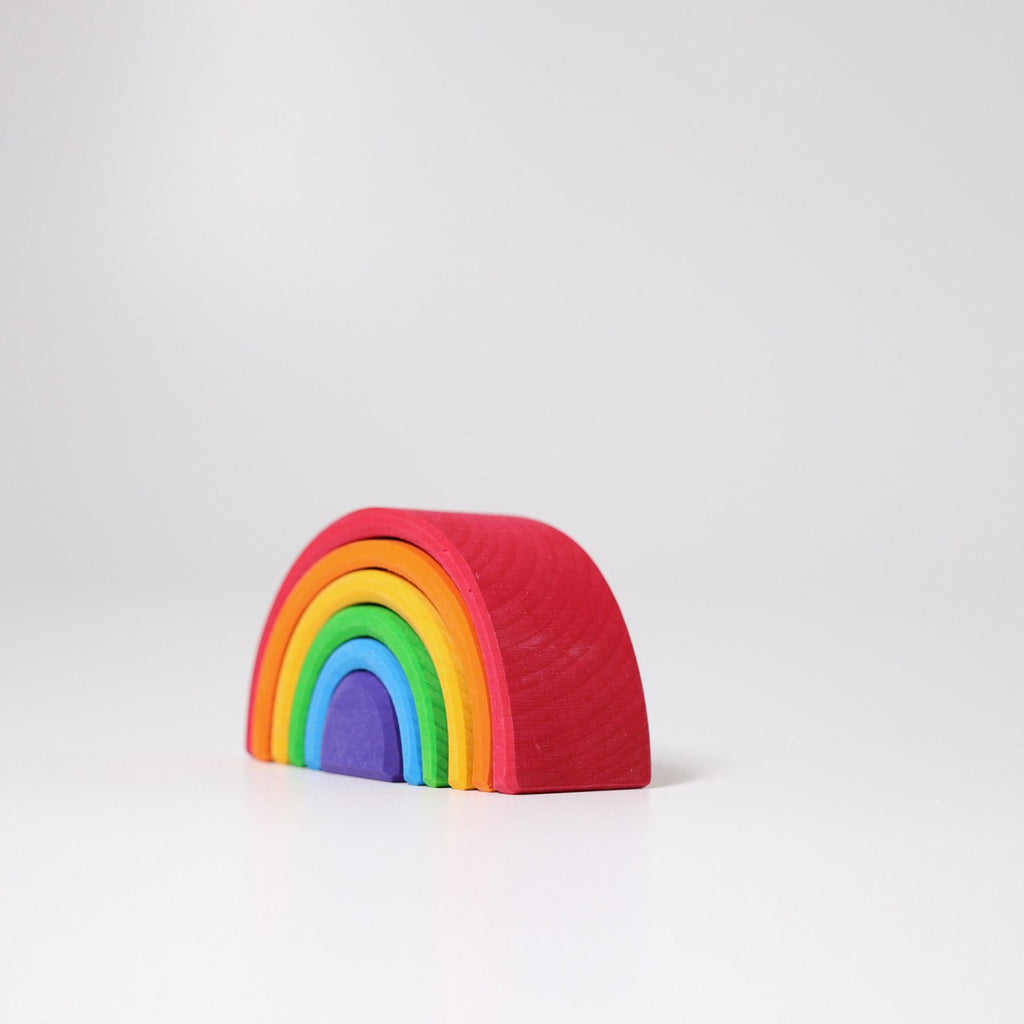 A versatile, minimalist wooden rainbow toy composed of seven stacked arches, each in a different color: red, orange, yellow, green, blue, indigo, and violet. Crafted from non-toxic wood, the Grimm's Small Wooden Rainbow stands against a plain white background.