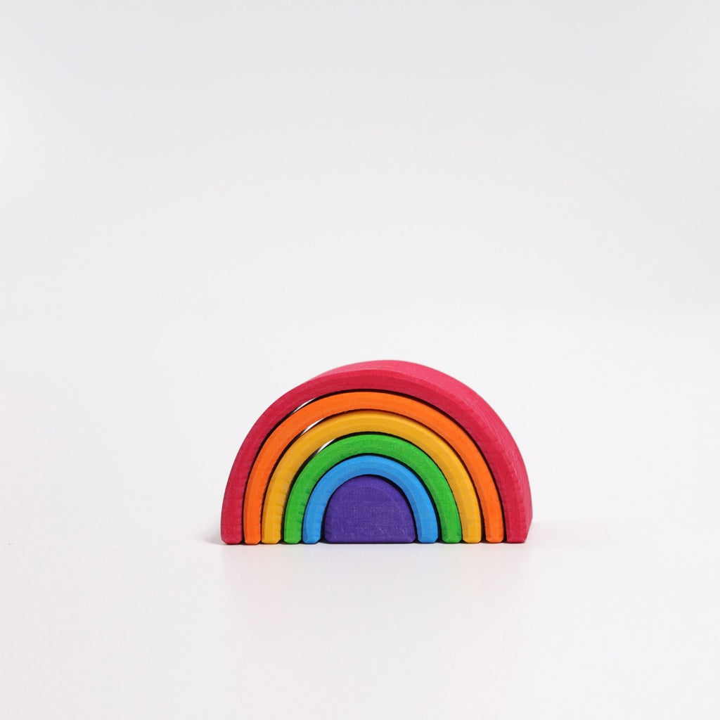 A Grimm's Small Wooden Rainbow set against a plain white background. The versatile toy is composed of seven concentric arches in colors red, orange, yellow, green, blue, indigo, and violet, stacked in a semi-circle shape and crafted from non-toxic wood.