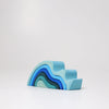 The Grimm's Ocean Waves, Small is a natural wood toddler stacking toy shaped like an abstract wave and painted in soothing blue shades, shown arranged on a white surface against a plain light background.