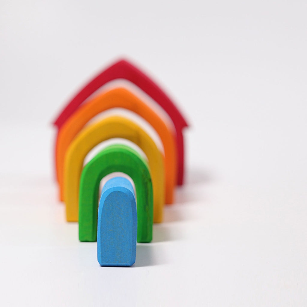 A series of colorful, arch-shaped wooden blocks are arranged in a line, decreasing in size from front to back. This non-toxic stacking toy features blocks in blue, green, yellow, orange, and red against a plain white background—perfect for toddlers' endless creativity. Introducing the Grimm's Colorful House Stacker!