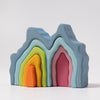 Grimm's Blue Cave Arch Stacking Toy features mountain-like wooden pieces in blue, pink, green, yellow, and orange with a natural oil finish, nested together on a plain white background.