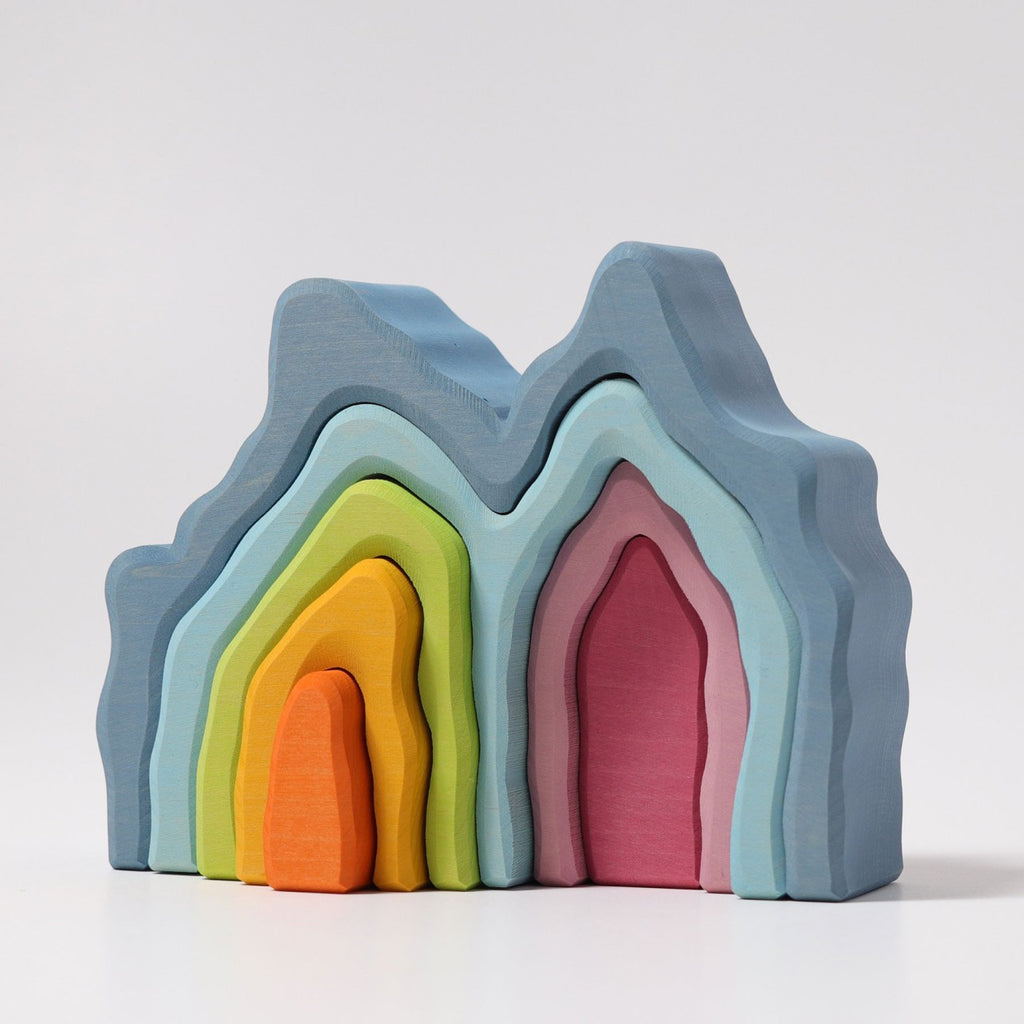 Grimm's Blue Cave Arch Stacking Toy features mountain-like wooden pieces in blue, pink, green, yellow, and orange with a natural oil finish, nested together on a plain white background.
