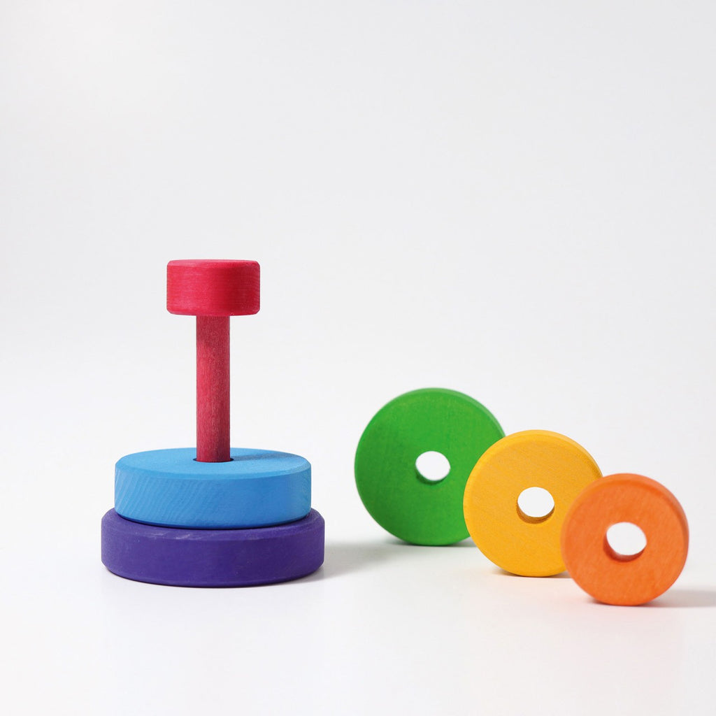 Grimm's Small Stacking Tower is a vibrant lime wood toy with a red post and colorful discs—blue, purple, green, yellow, and orange—perfect for developing fine motor skills as kids stack or sort on a white background.