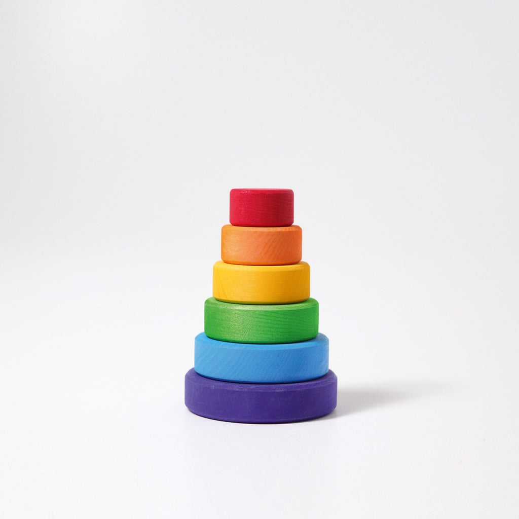 Grimm's Small Stacking Tower features six colorful lime wood discs, arranged by size from largest (purple) to smallest (red), to help develop fine motor skills—displayed on a plain white background.