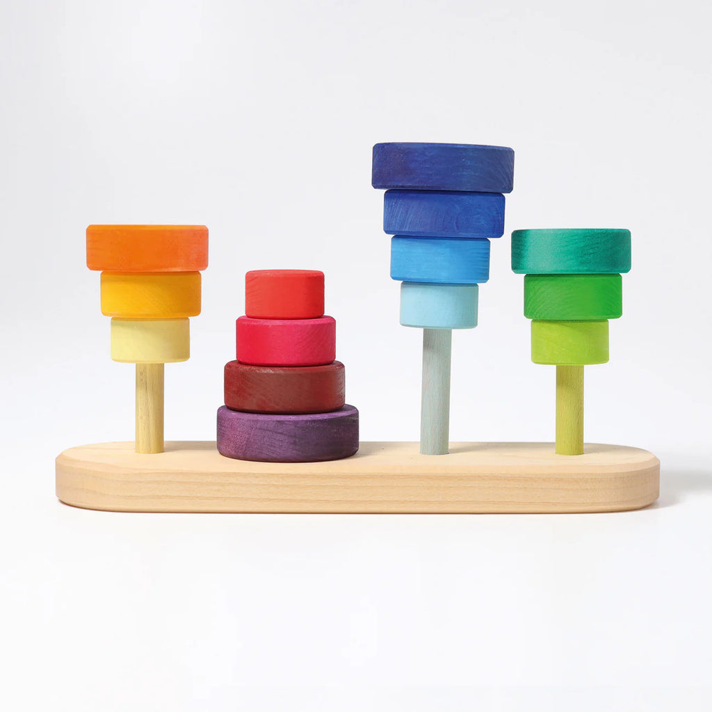Grimm's Fabuto Stacker: a wooden stacking toy with vibrant red, yellow, blue, and green disks on four pegs atop a light wood base—ideal for color coordination and classic play.