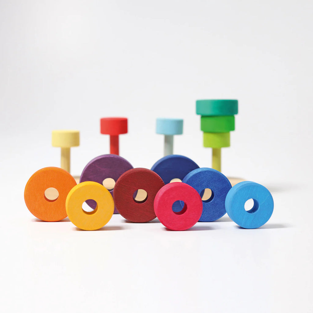 Grimm's Fabuto Stacker features colorful wooden rings in yellow, red, blue, green, and purple on vertical pegs. The vibrant design encourages playful color coordination and sorting activities.