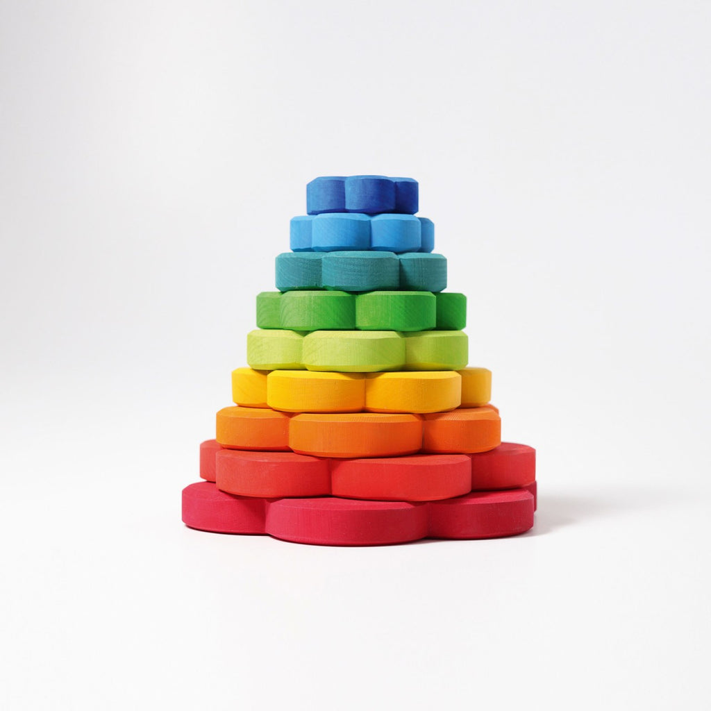 Introducing Grimm's Flower Stacking Tower: a vibrant children's stacking toy featuring a blue central peg. The non-toxic pieces come in various colors and sizes, from small blue and green flowers to larger red, orange, and yellow blooms. Each flower boasts multiple holes that encourage the development of fine motor skills as they are arranged around the peg.