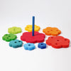 Introducing Grimm's Flower Stacking Tower: a vibrant children's stacking toy featuring a blue central peg. The non-toxic pieces come in various colors and sizes, from small blue and green flowers to larger red, orange, and yellow blooms. Each flower boasts multiple holes that encourage the development of fine motor skills as they are arranged around the peg.