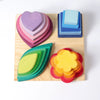 Grimm’s Stacking Game Shapes featuring four sets of wooden nesting shapes in heart, square, leaf, and flower patterns arranged on a square base as a fine motor skills stacking toy.