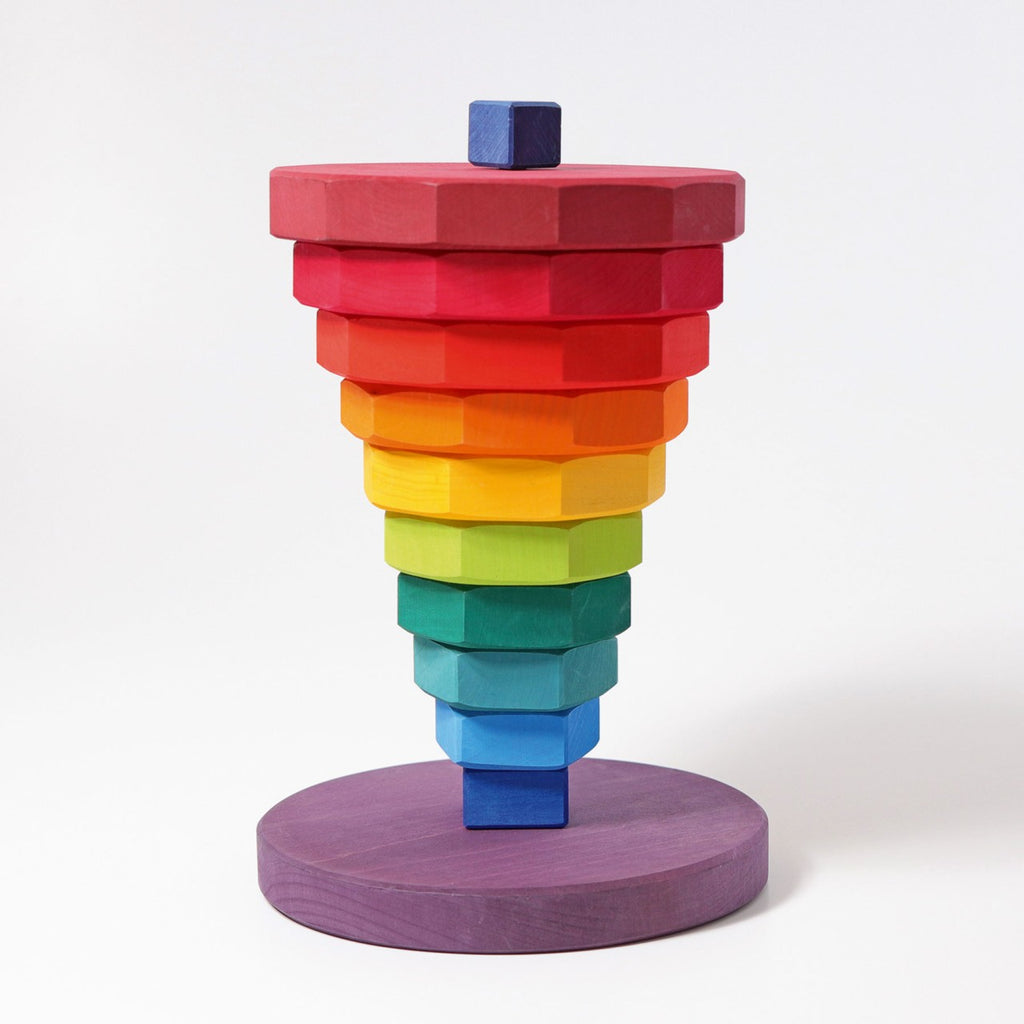 Grimm's Giant Geometrical Stacking Tower is a colorful wooden stacking toy consisting of hexagonal blocks arranged in a pyramid shape. Crafted from non-toxic wood, the blocks are painted in a gradient of rainbow colors, from red at the top to purple at the bottom, and sit on a circular purple base—a perfect fine motor skills toy.