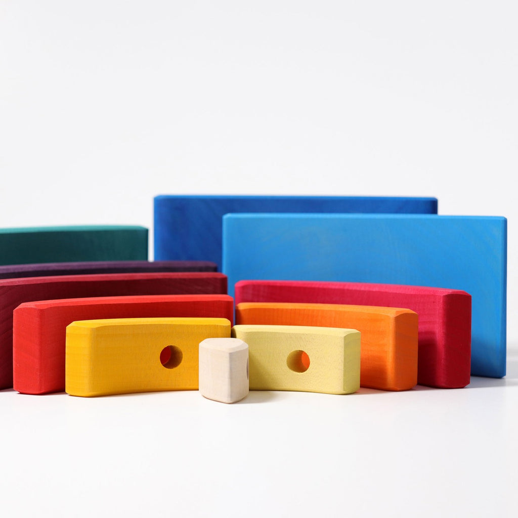 Grimm's Stacking Tower Sailboat features colorful wooden blocks in various shapes, including rectangles and curved pieces with holes, arranged on a white surface to encourage fine motor skill development.
