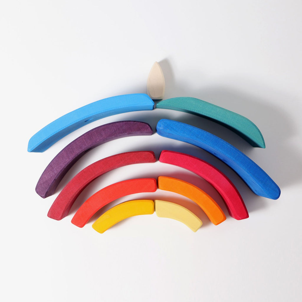 Grimm's Stacking Tower Sailboat features colorful wooden arches and a small flame-shaped piece, stacked on a white surface to form a stylized rainbow with a central flame—ideal for enhancing fine motor skills.