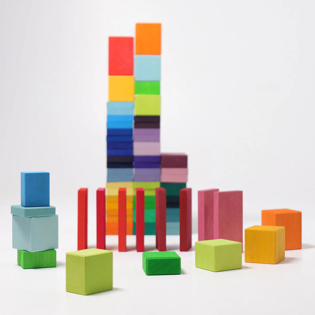 Grimm's Color Charts-Rally features vibrant stained wood tiles and blocks in different shapes and sizes, stacked on a white surface with taller stacks behind smaller blocks—ideal for building fine motor skills.