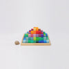 The Grimm's Stepped Pyramid Block Set - Small features colorful wooden blocks arranged in a gradient on a square tray, with a small brown snail shell to the left, all displayed on a white background.