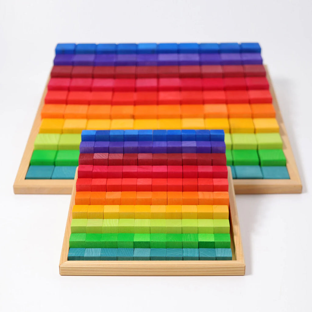 Two wooden trays, each filled with Grimm's Stepped Counting Blocks - Small (coming soon), display non-toxic rainbow blocks arranged in vibrant order from red to blue, with one tray slightly in front of the other on a white surface.