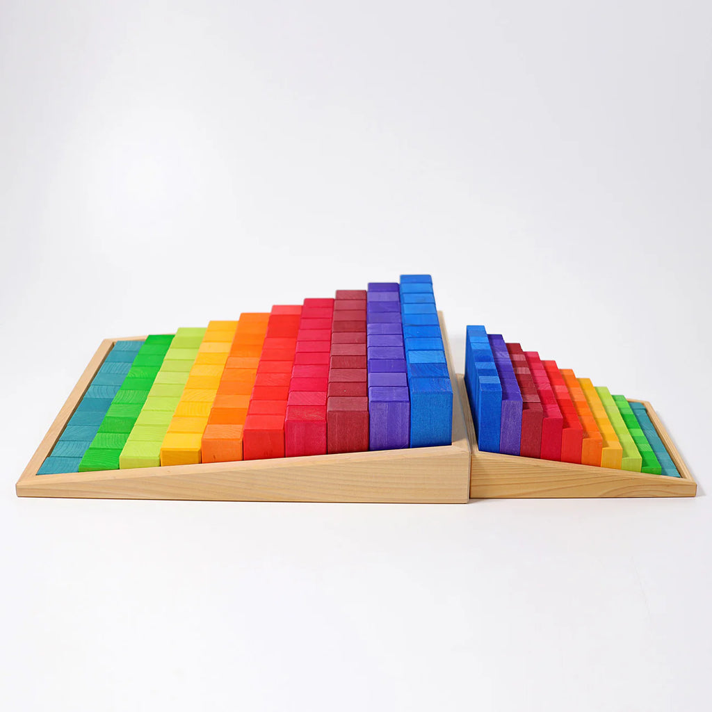 Grimm's Stepped Counting Blocks - Small (coming soon) features two sets of wooden blocks in triangular prisms, painted with a green-to-red-to-purple rainbow gradient for vibrant, creative play. Non-toxic and perfect on a white background.