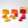 Grimm’s Sorting Game Rainbow Bowls with Tweezers featuring three wooden bowls in yellow, orange, and red arranged behind a collection of matching small wooden fish, heart, and star shapes for a color sorting game.