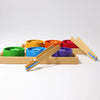 Grimm’s Sorting Game Rainbow Bowls with Tweezers featuring six colorful wooden bowls in a sorting tray, each containing a matching wooden star, with two wooden tweezers resting nearby for fine motor skills.