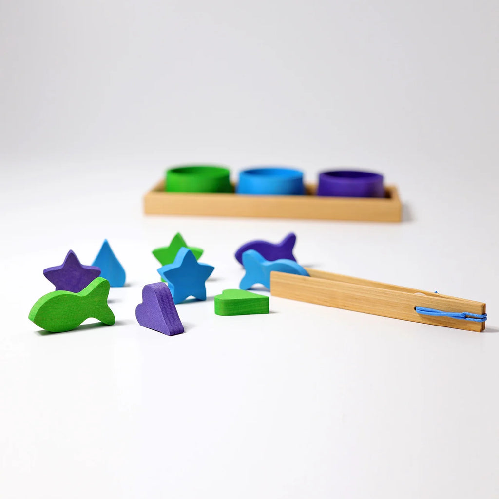Grimm’s Sorting Game Rainbow Bowls with Tweezers featuring wooden tweezers, small wooden bowls, and colorful geometric and animal-shaped pieces arranged on a white surface for a sorting activity.