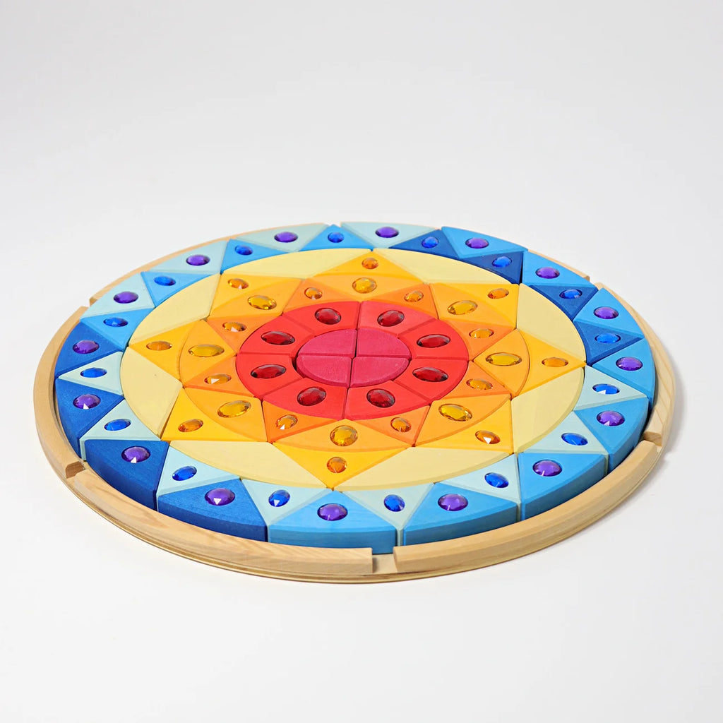Grimm’s Sparkling Mandala Sun Creative Puzzle featuring circular wooden pieces arranged in a radiating pattern with colorful inlaid acrylic gemstones for fine motor skill development.